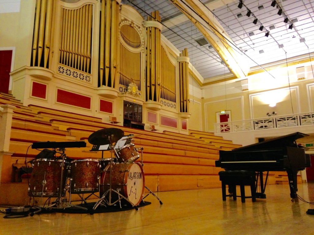 De Montfort Hall concert stage with pipe organ, piano and drum set.