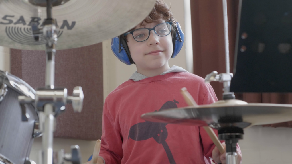 Student wearing ear defenders playing drums.